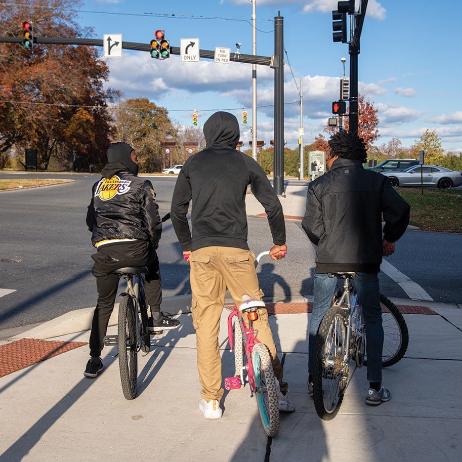 Three young black men on bicycles wait to cross Auchentoroly Terrace