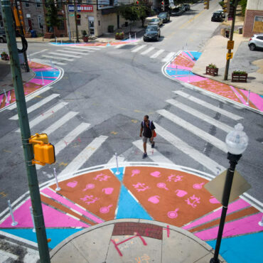 Pigtown Iconic at Washington & Cross feature image birds eye view of man crossing the street framed by bright pink, brown, and blue crosswalk bump outs.