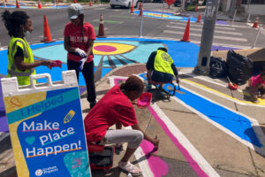 Oliver Allover Eyes community paint day Make Place Happen sign and people painting the sidewalk