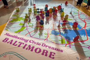 Manifesting Civic Dreams Baltimore map with golden hour shadows cast by colorful pop-up signs