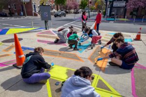 Patterson Plumage community paint day perspective view with local youth painting the sidewalk entrance to Patterson Park