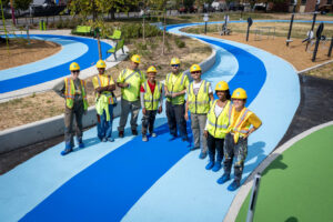 Cecil Community Park: birds eye view of the Graham Projects installation team wearing safety vests and construction helmets, standing on curvilinear blue and turquoise pavement art covered walking track.