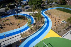 Cecil Community Park: birds-eye view facing north east featuring curvilinear blue and turquoise pavement art walking tracks, landscaping, and playgrounds.