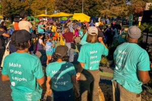 Damascus Placemaking Festival perspective view of residents in amphitheater participating in dancing performance with colorful scarves and Graham Projects team in foreground wearing bright teal "MAKE PLACE HAPPEN" t-shirts