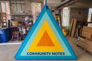 Lortz Lane LortzWave shared street perspective view of triangular kiosk front with concentric triangular colors bands orange, yellow, light teal, dark teal, blue, and the words "COMMUNITY NOTES" in black