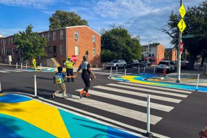 Franklin Square EMS Heraldic Bands perspective of crossing guard helping a mother an son cross the street