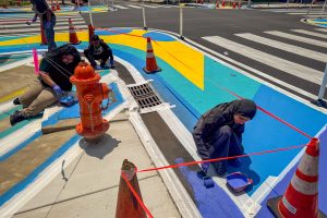 Franklin Square EMS Heraldic Bands installation perspective of students painting the sidewalk and street