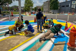 Franklin Square EMS Heraldic Bands installation perspective of Graham and Melvin helping guiding students painting the sidewalk