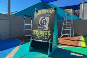 2700 Art Space ministage with chalkboard inviting the public to "Wheatpaste the Inner Ear Tribute Wall"
